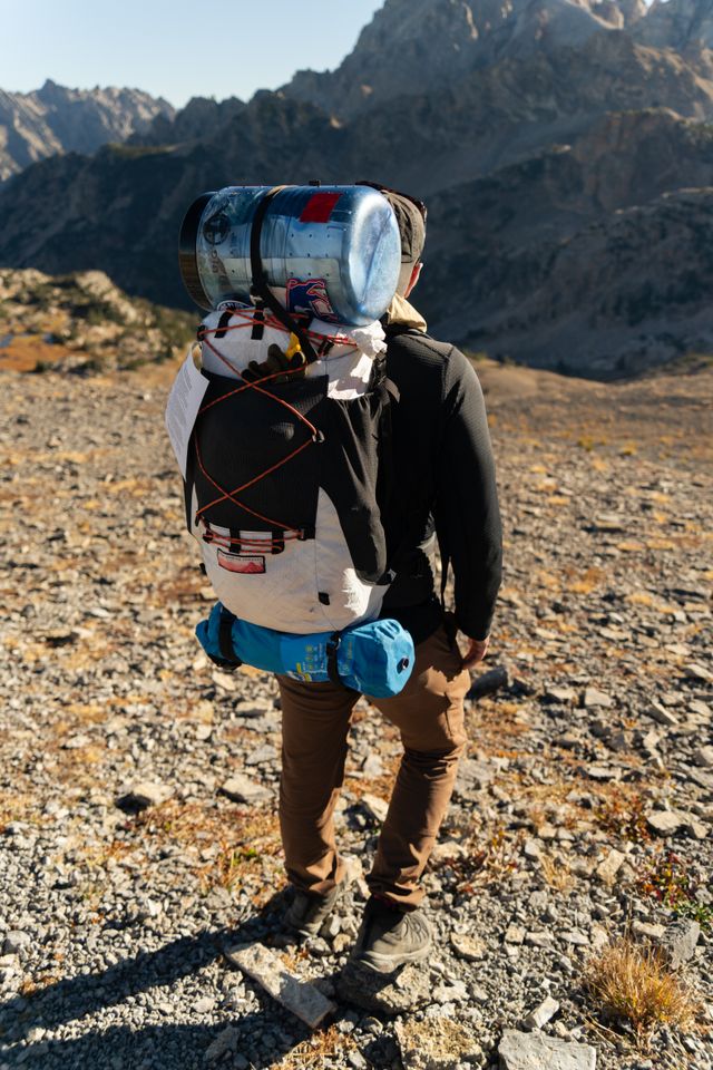 A backpacker on a rocky mountain trail facing rugged peaks